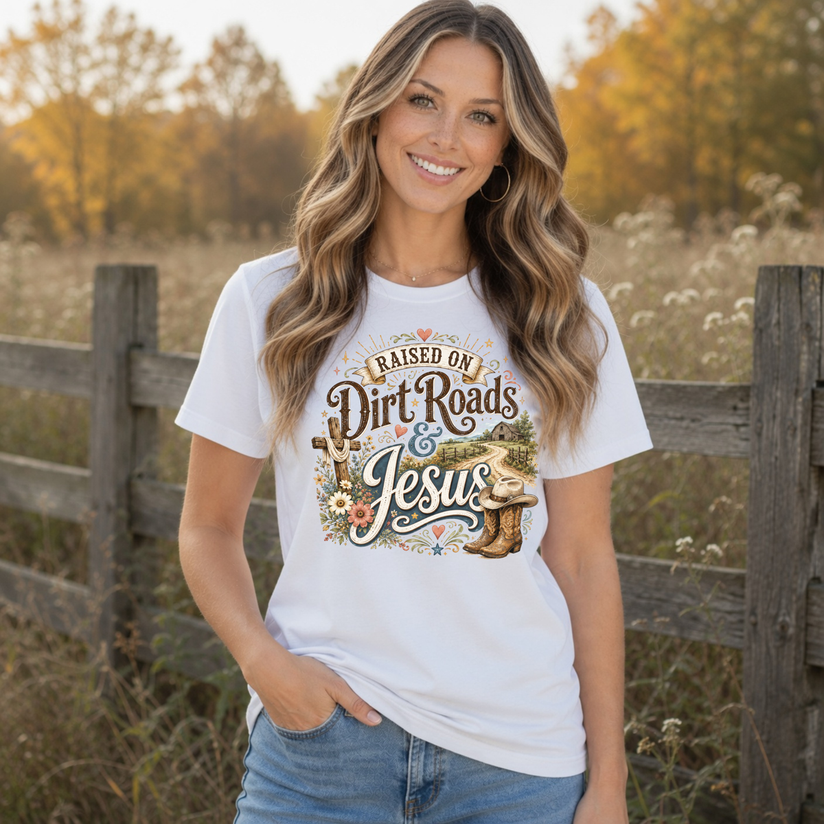Woman wearing a white Raised on Dirt Roads & Jesus T-shirt in a warm country field setting.