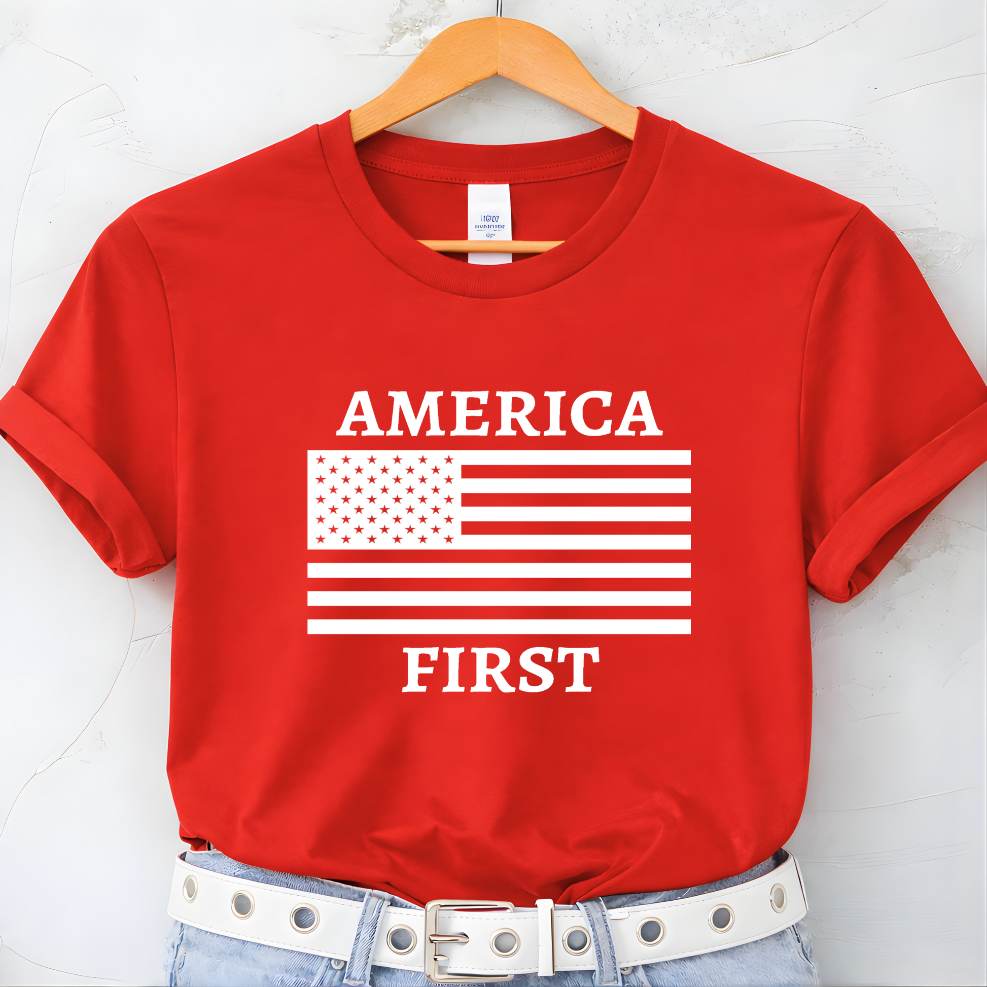 Red t-shirt with 'AMERICA FIRST' text and American flag design on a hanger.