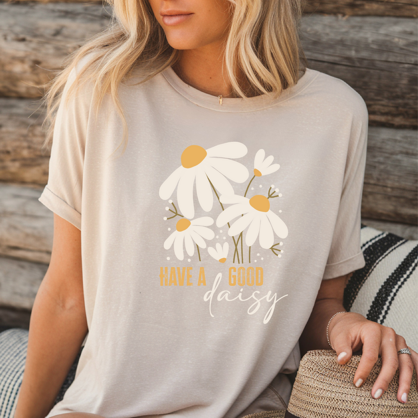 Woman wearing a beige t-shirt with daisy design and text 'Have a good daisy' against a wooden background.
