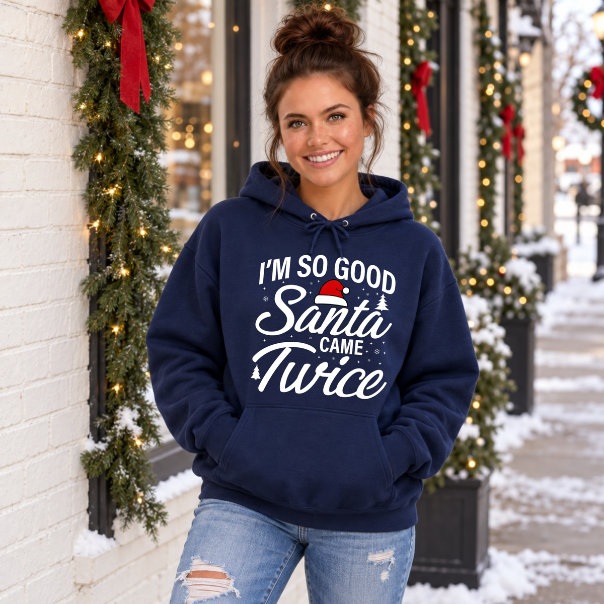 Woman modeling a navy hoodie with the Santa Came Twice Christmas graphic in a snowy holiday scene.