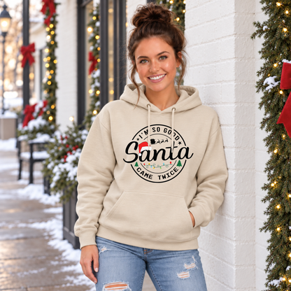 Woman wearing a sand hoodie with I'm So Good Santa Came Twice Christmas design outside a snowy decorated storefront