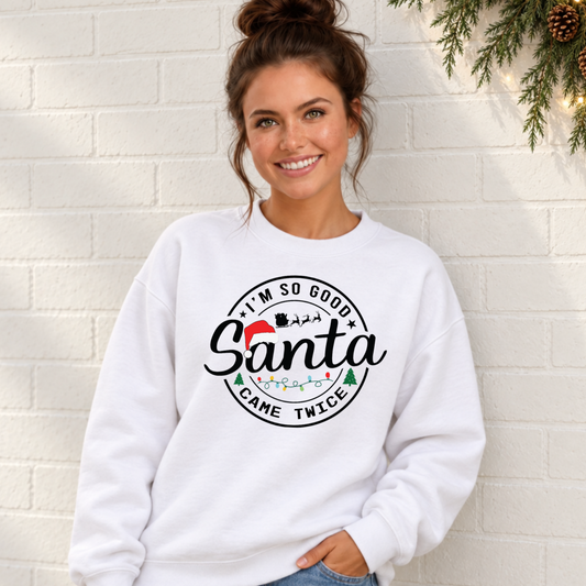 Woman wearing a white sweatshirt with I'm So Good Santa Came Twice Christmas design against a white brick wall