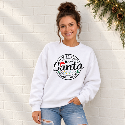 Woman wearing a white sweatshirt with I'm So Good Santa Came Twice Christmas design against a white brick wall