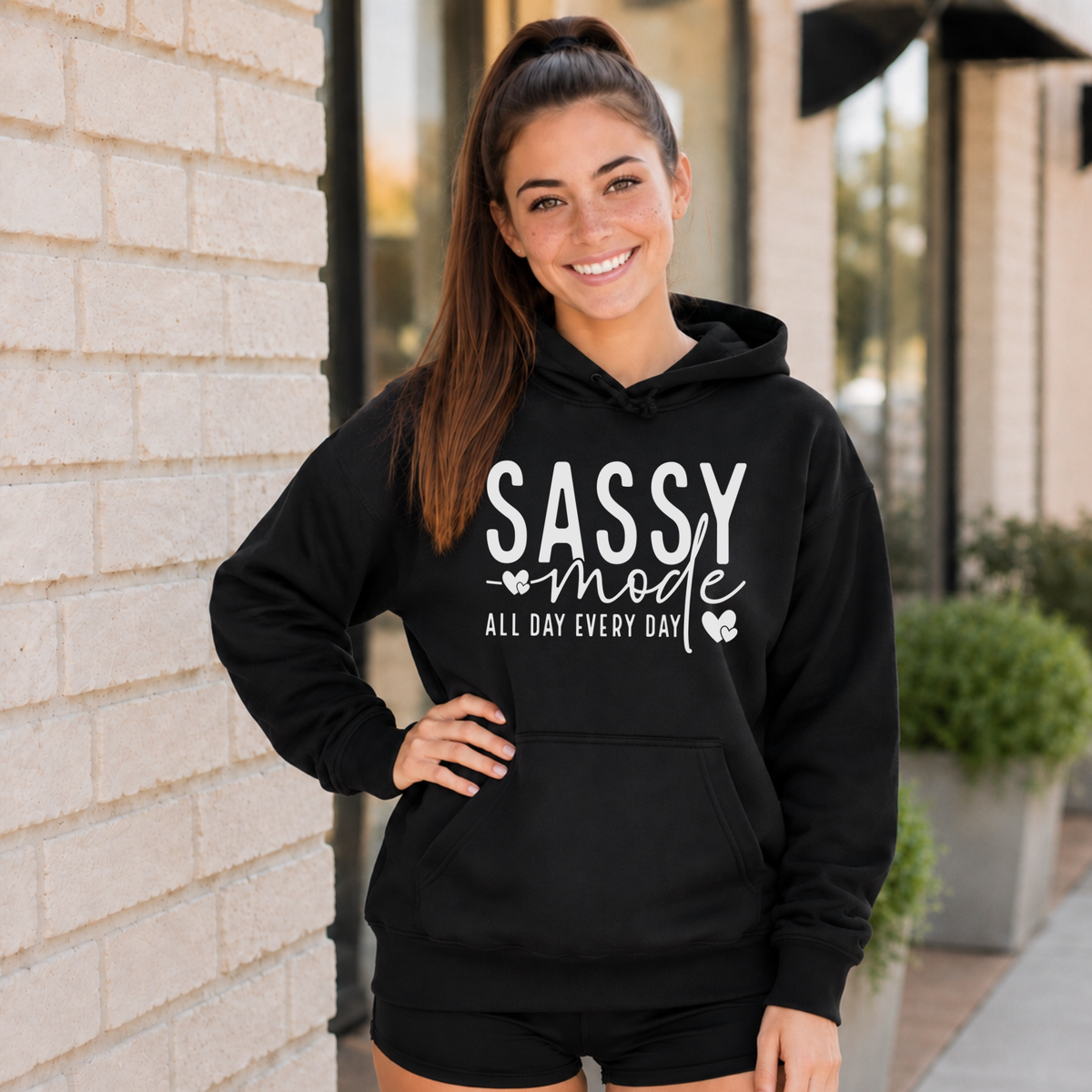 Woman wearing a black Sassy Mode hoodie with white lettering outside a storefront.
