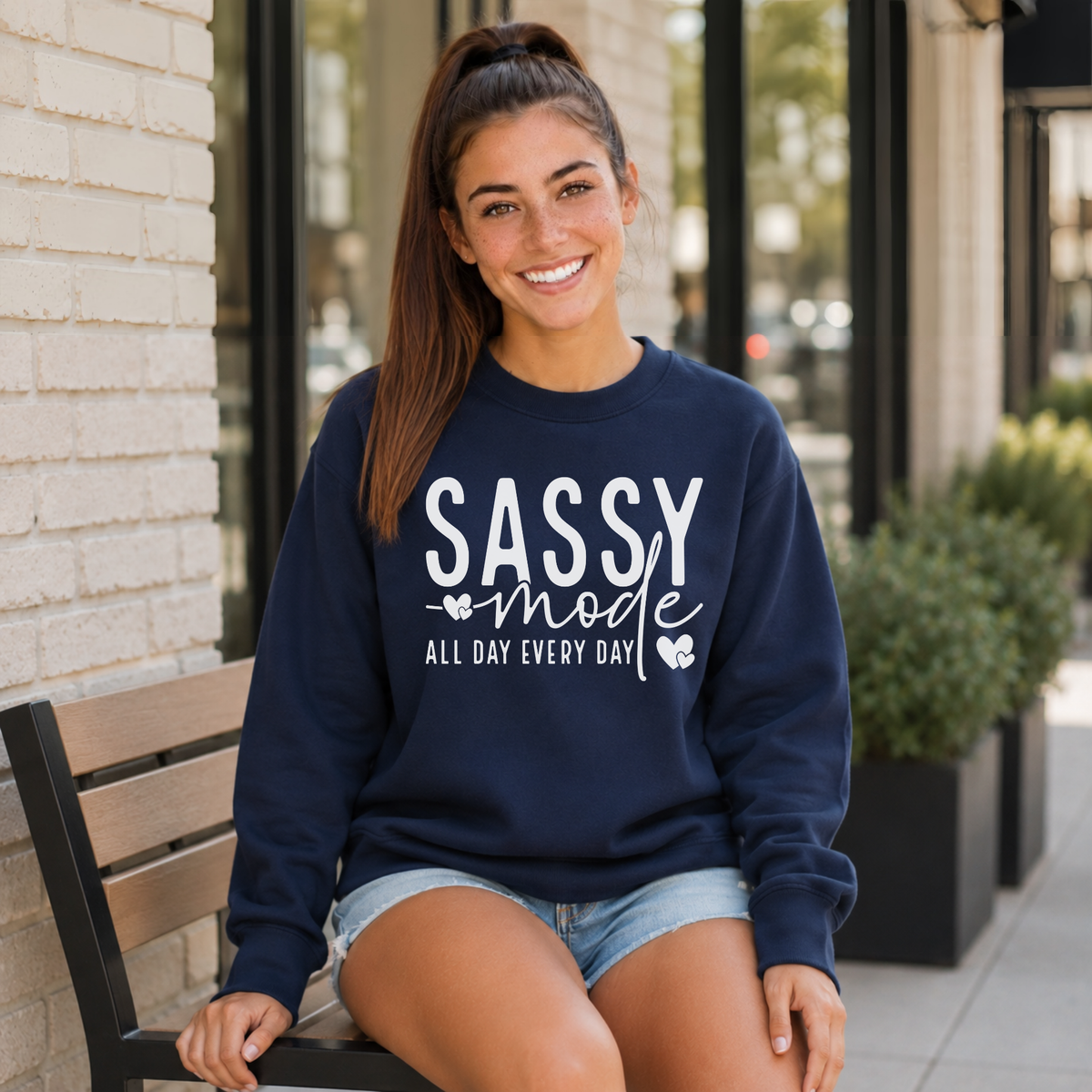 Woman wearing a navy Sassy Mode sweatshirt with white lettering while seated outside a storefront.