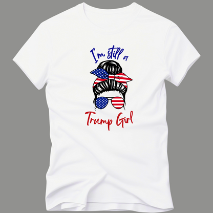 Woman wearing pink “I’m Still a Trump Girl” patriotic T-shirt with USA flag bun and sunglasses design.