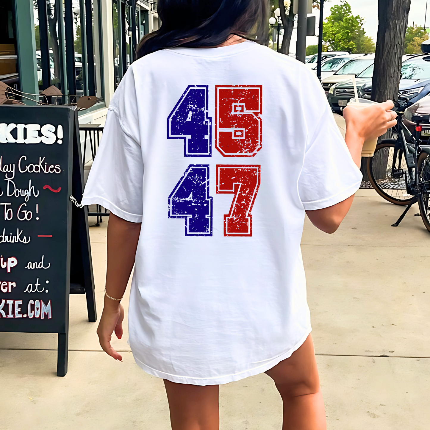 Person wearing a white t-shirt with red and blue numbers on the back, standing outdoors.