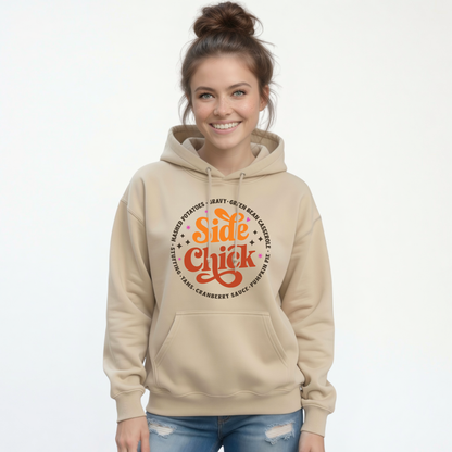 A smiling woman with her hair in a bun wears a Sand pullover hoodie featuring the retro “Side Chick” Thanksgiving graphic with dark side-dish lettering, paired with blue jeans on a white background.