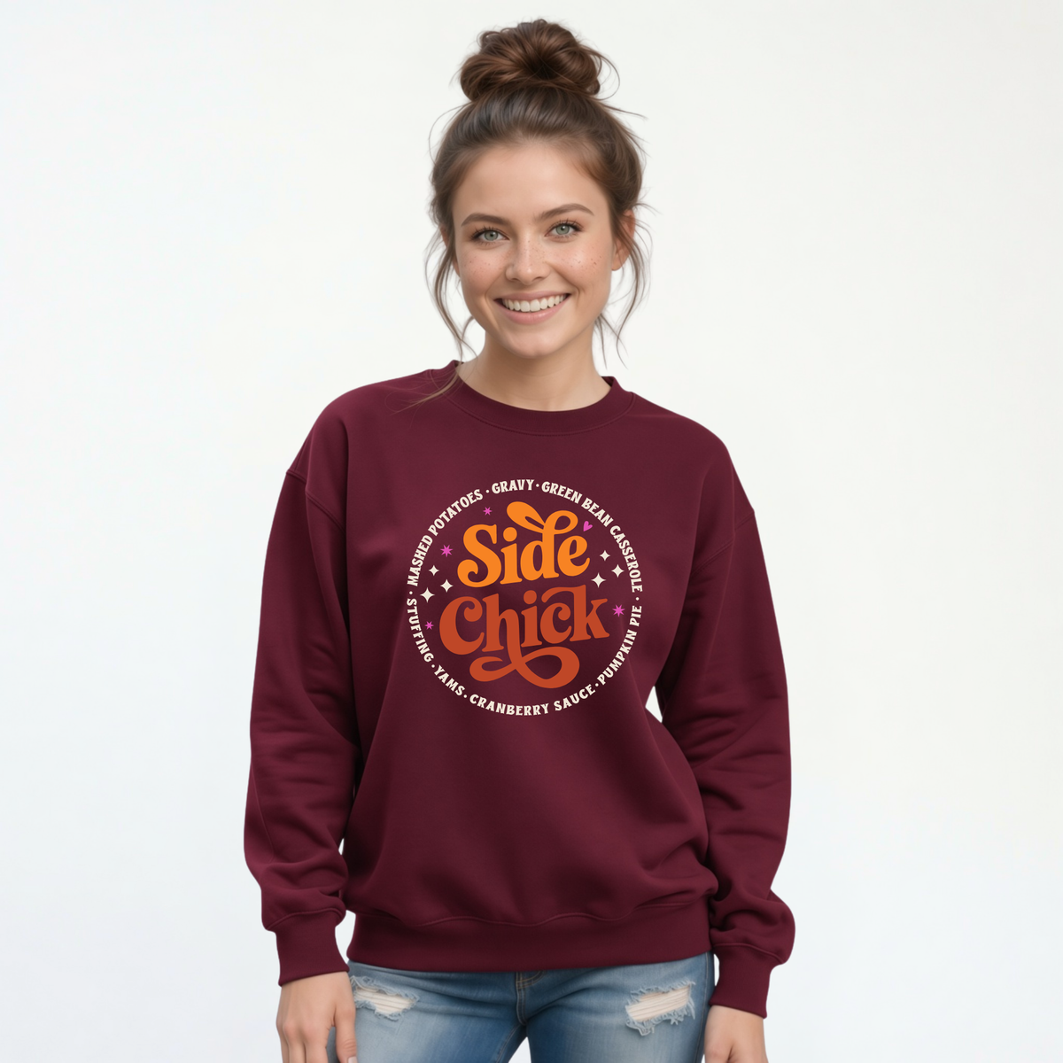 A woman models a Maroon crewneck sweatshirt with a retro orange-and-light “Side Chick” Thanksgiving graphic, styled with distressed jeans against a white background.