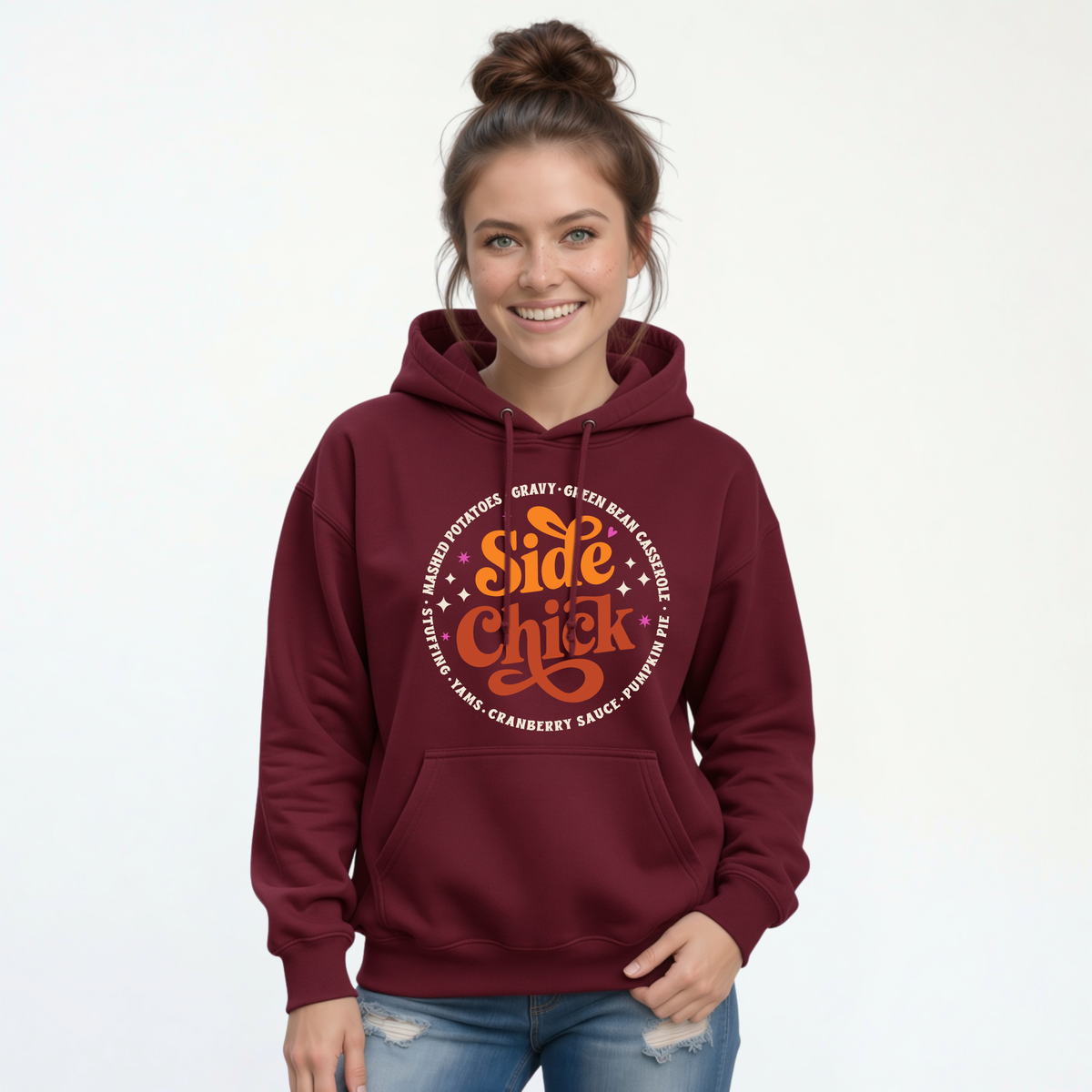A woman models a Maroon pullover hoodie with the bold “Side Chick” Thanksgiving graphic and light circular side-dish text, paired with jeans against a white background.