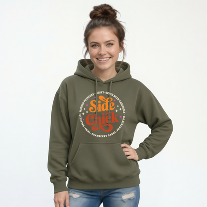 A woman wears a Military Green pullover hoodie featuring the retro “Side Chick” Thanksgiving design with bright lettering and side-dish names against a clean white background.