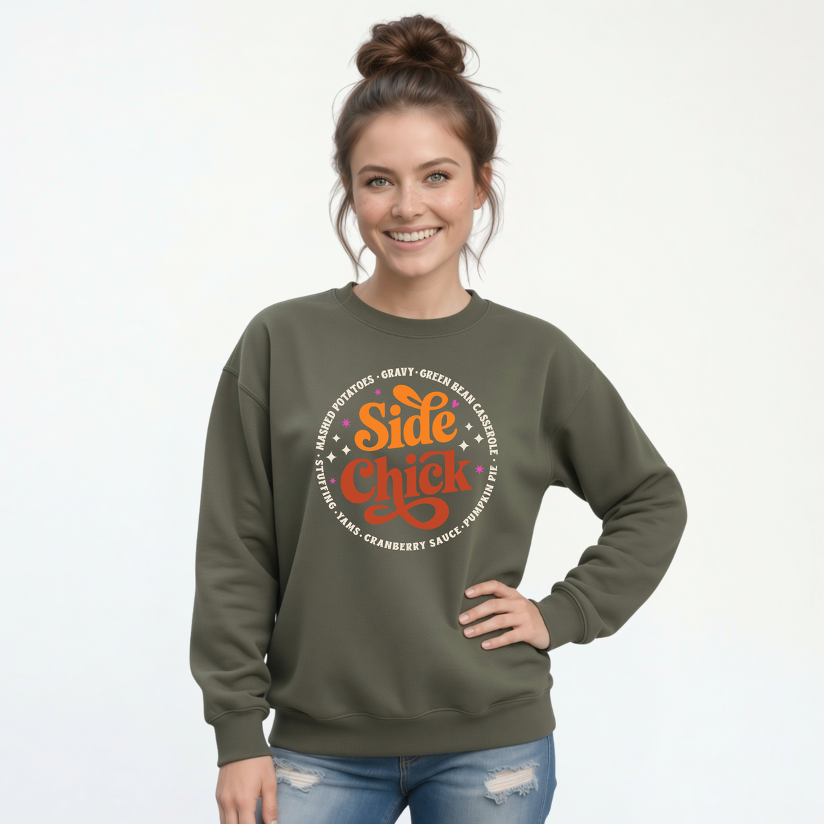 A woman wears a Military Green crewneck sweatshirt with the retro “Side Chick” Thanksgiving design and light side-dish lettering, paired with blue jeans on a white studio background.