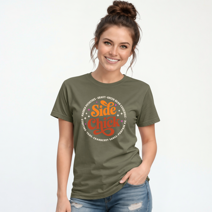 A woman models a Military Green T-shirt with the funny “Side Chick” Thanksgiving graphic, bright circular lettering, and retro star accents against a white background.