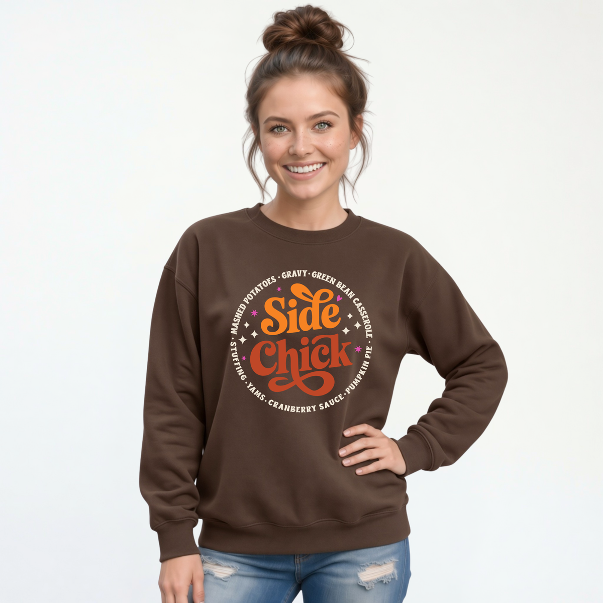 A woman wears a Brown crewneck sweatshirt featuring the bold “Side Chick” Thanksgiving graphic with light side-dish lettering, styled with jeans against a white background.