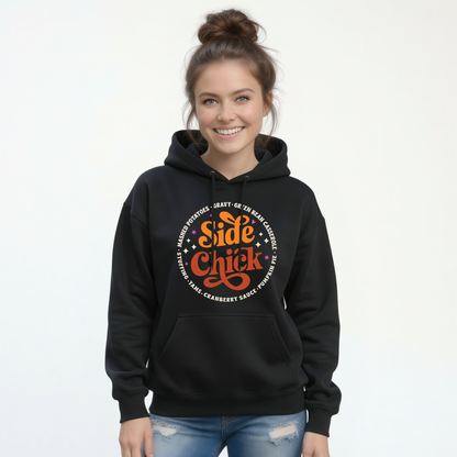 A woman models a Black pullover hoodie with the bold retro “Side Chick” Thanksgiving graphic and light circular side-dish lettering, paired with blue jeans against a clean white background.