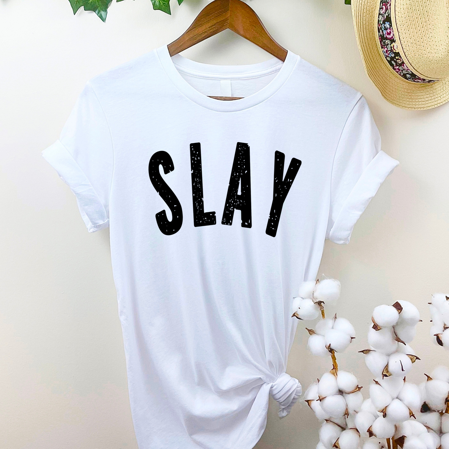 White t-shirt with 'SLAY' text on a hanger with decorative elements.
