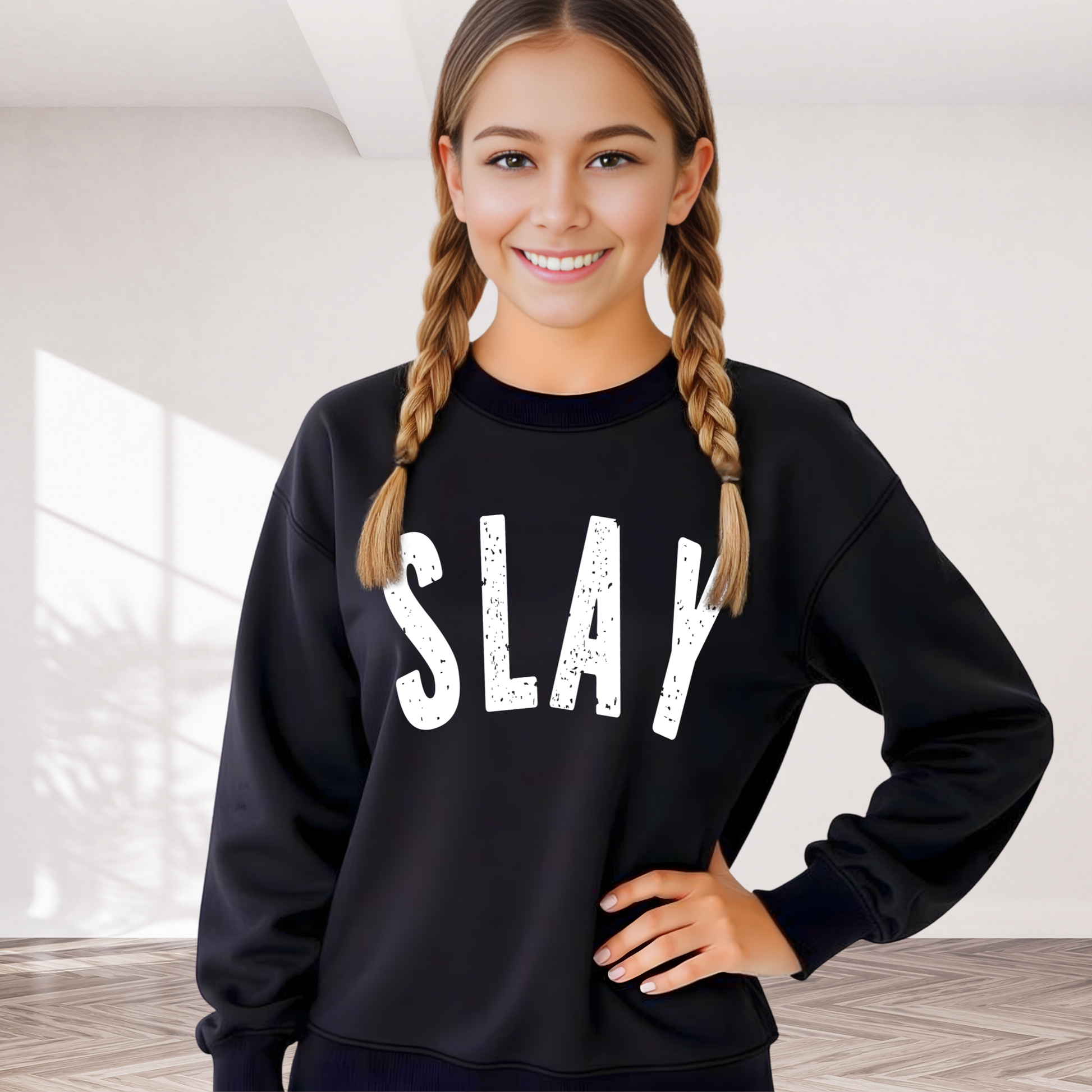 Teen girl wearing a black sweatshirt with 'SLAY' printed on it, standing in a bright room.
