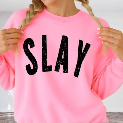 Person wearing a pink sweatshirt with 'SLAY' printed in black letters.