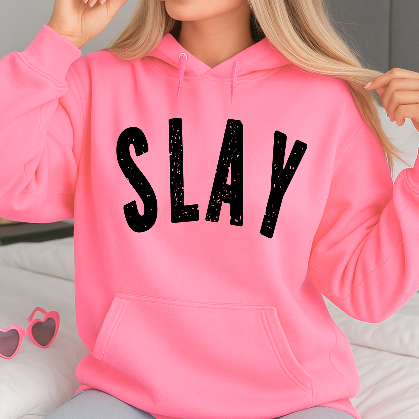 Person wearing a pink hoodie with 'SLAY' text, sitting on a light-colored surface.