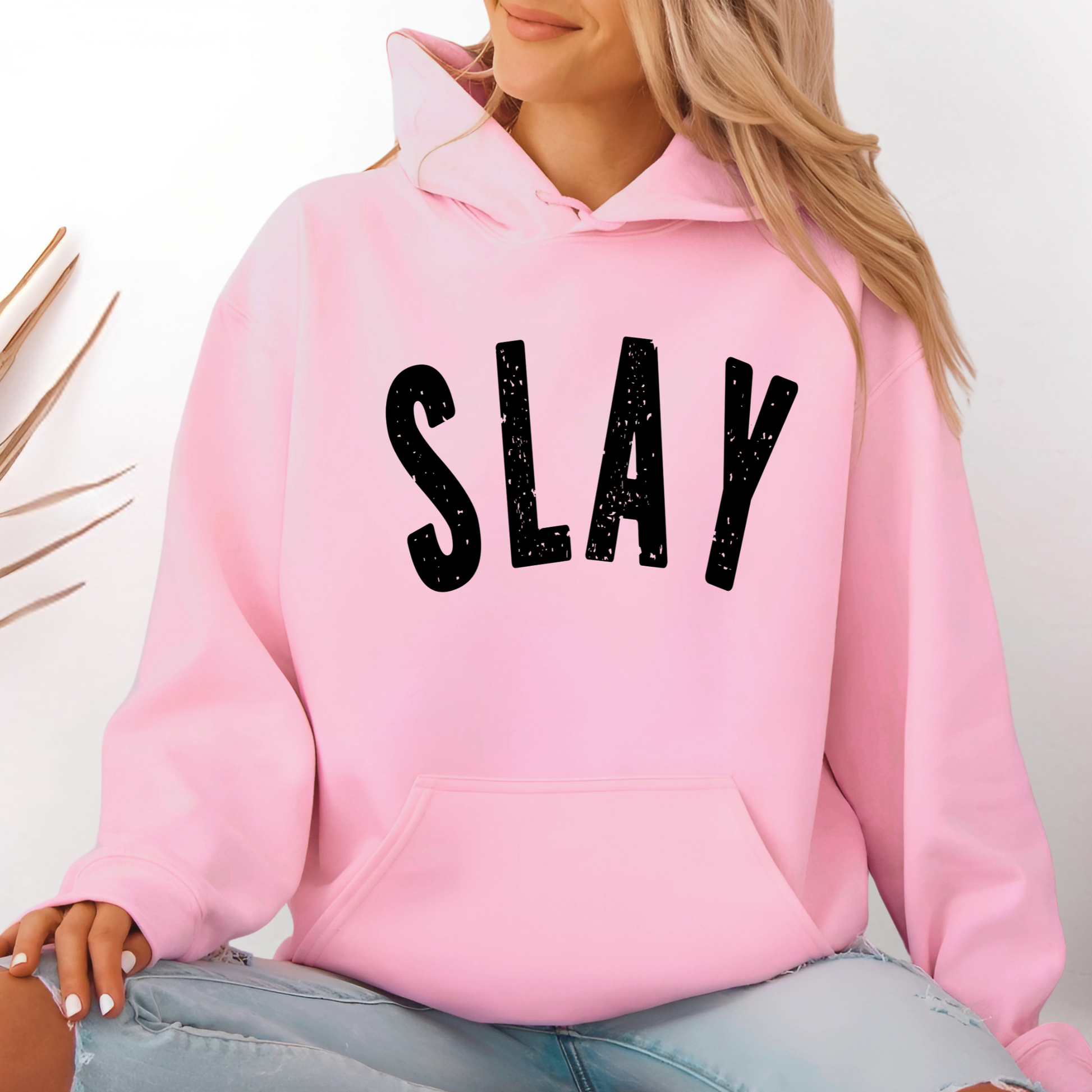 Pink hoodie with 'SLAY' text worn by a Woman, against a neutral background