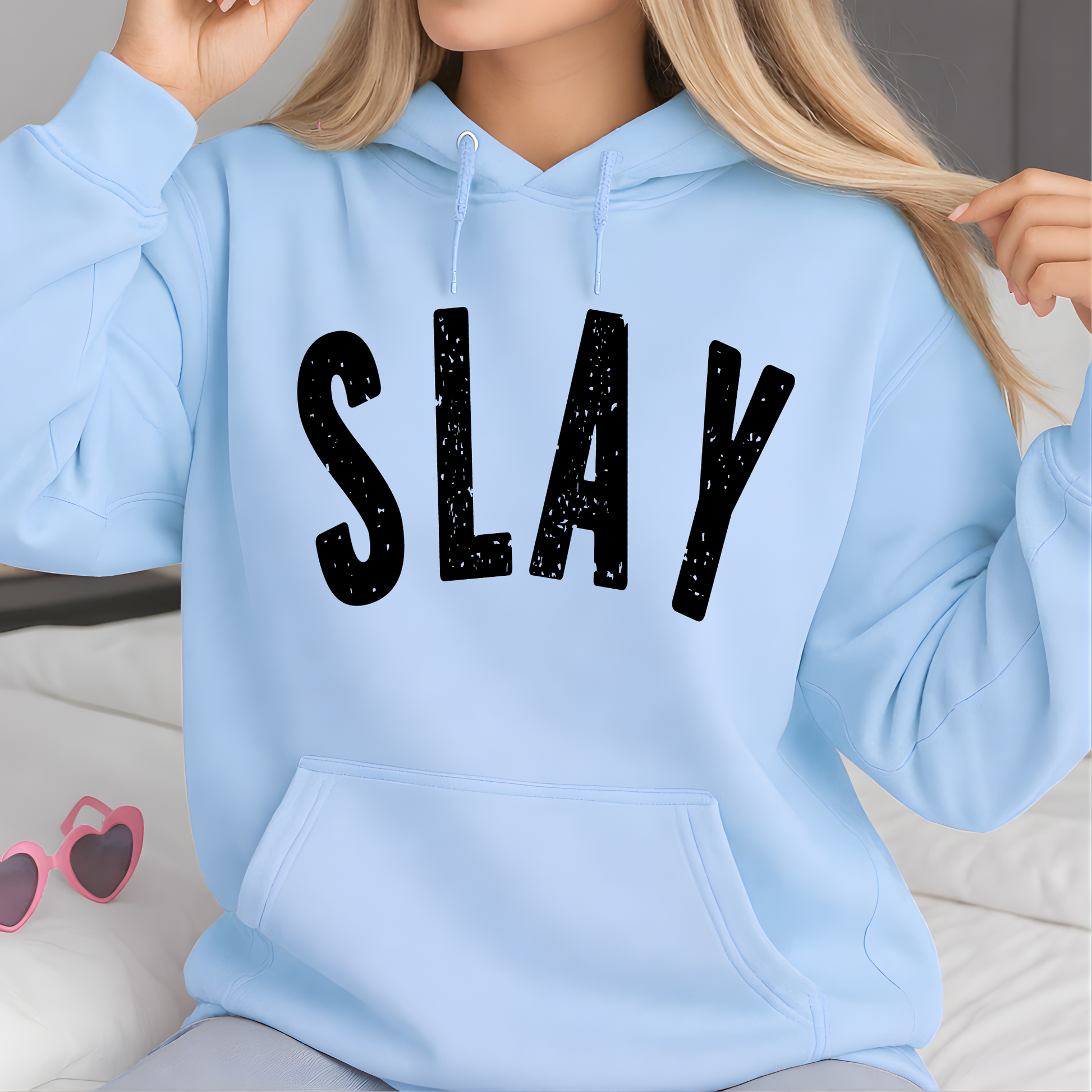 Light blue hoodie with 'SLAY' text worn by a person, with sunglasses in the background.
