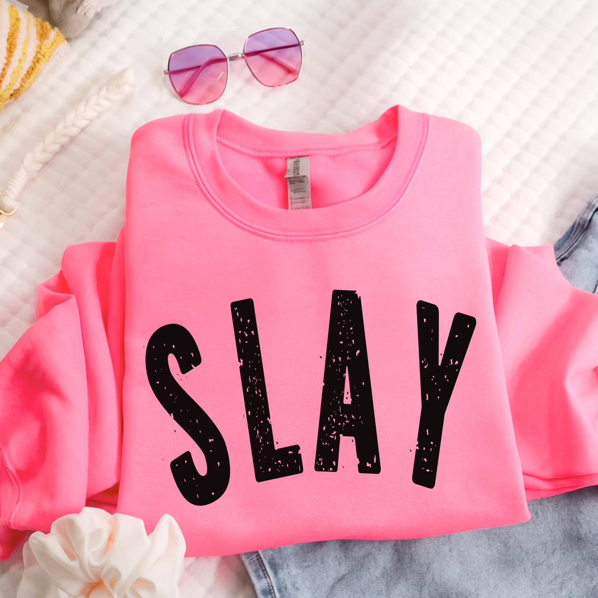 Flat lay bright pink SLAY sweatshirt folded with sunglasses and denim
