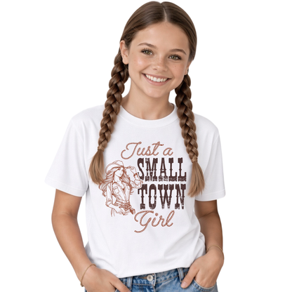 Smiling young female model with long braided hair wearing a white youth T-shirt with the “Just a Small Town Girl” western cowgirl graphic, paired with blue jeans against a clean white background.