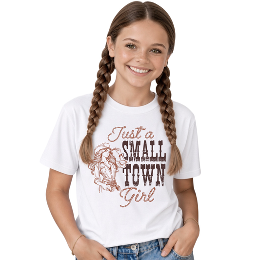 Smiling young female model with long braided hair wearing a white youth T-shirt with the “Just a Small Town Girl” western cowgirl graphic, paired with blue jeans against a clean white background.