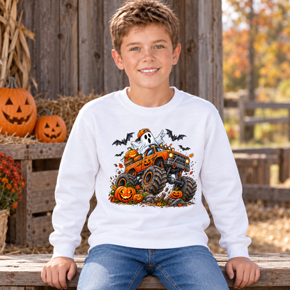 Smiling boy seated in a white youth crewneck sweatshirt with an orange Halloween monster truck, friendly ghost, jack-o-lanterns, and bats at a decorated fall farm stand.