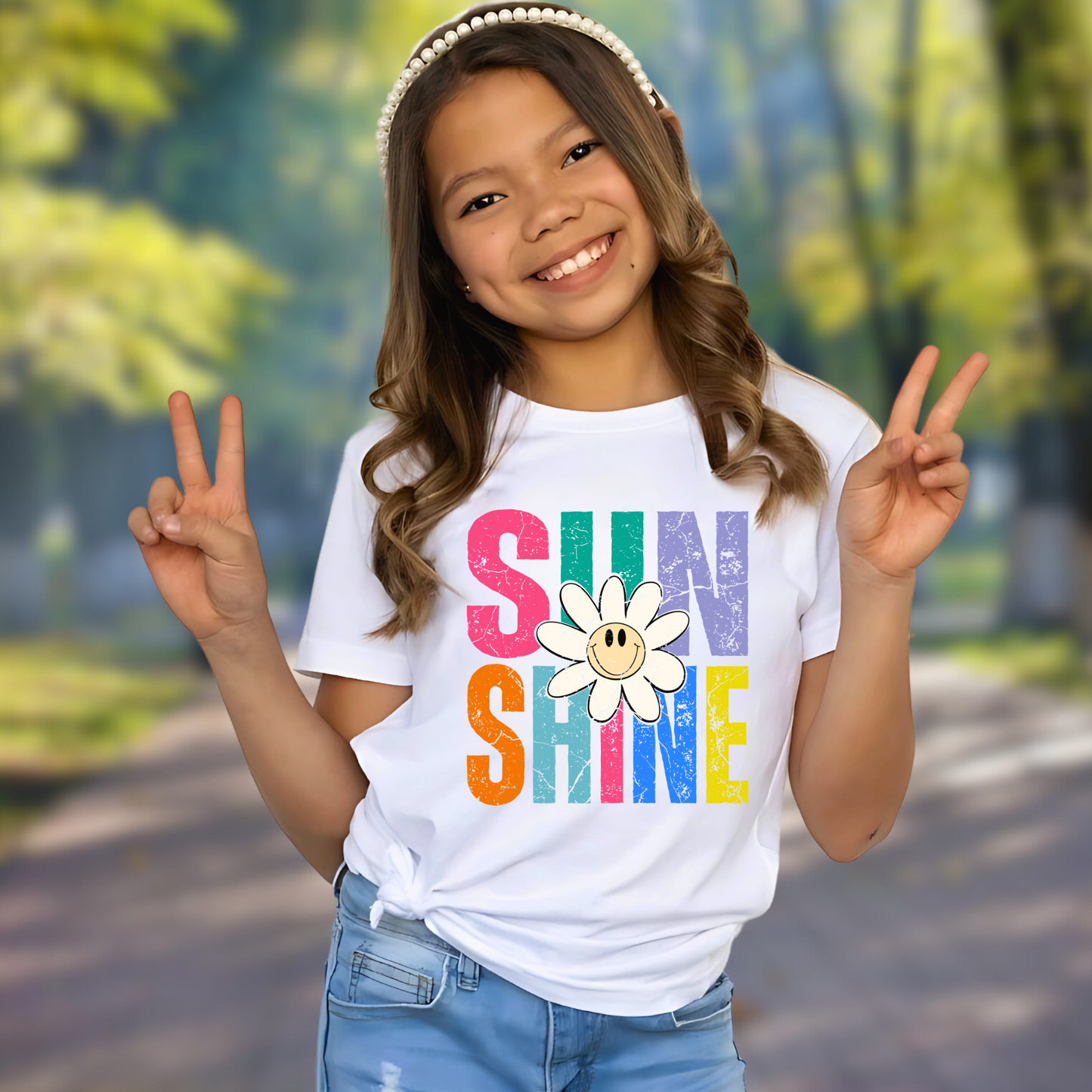 Smiling girl outdoors in a white Sunshine graphic tee, flashing peace signs with colorful rainbow print and happy daisy

