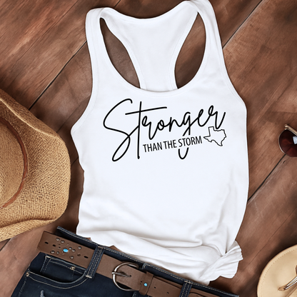 White tank top with 'Stronger Than The Storm' text on a wooden surface with accessories. Texas flood relief tank top