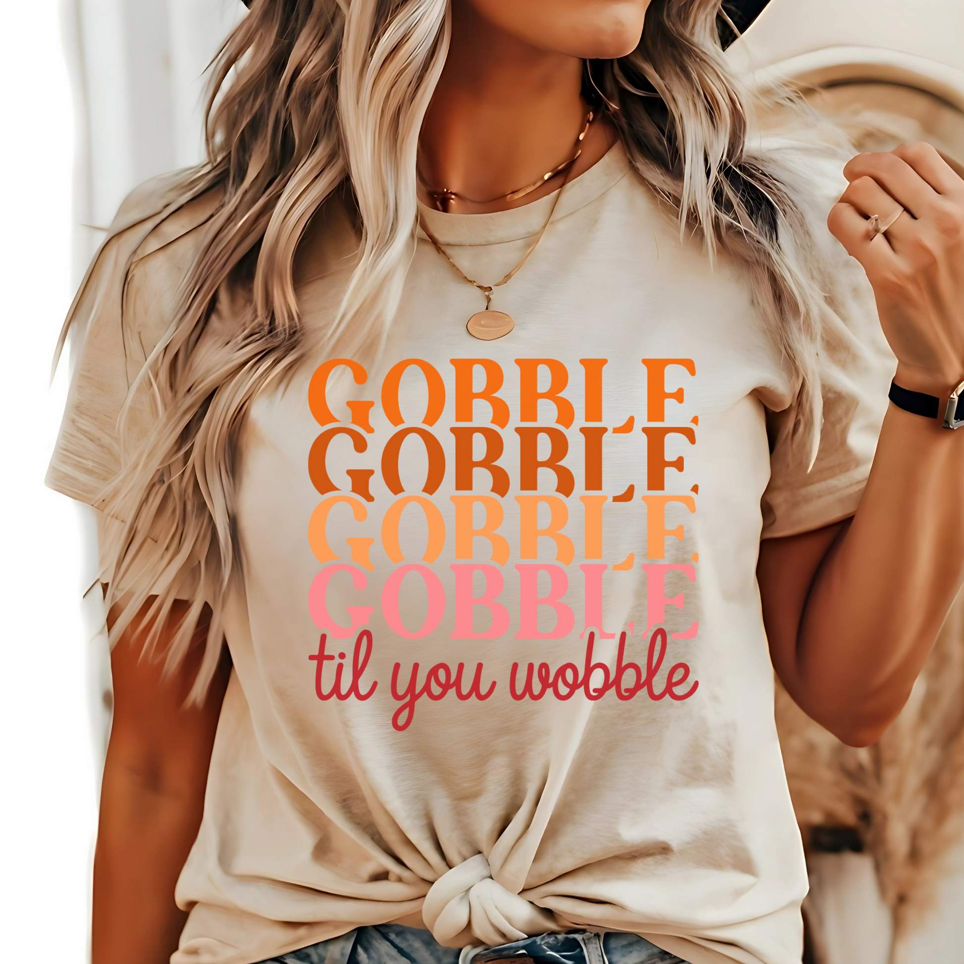 Stylish woman outdoors wearing a sand-colored knotted t-shirt with festive “Gobble Til You Wobble” design, accessorized with jewelry