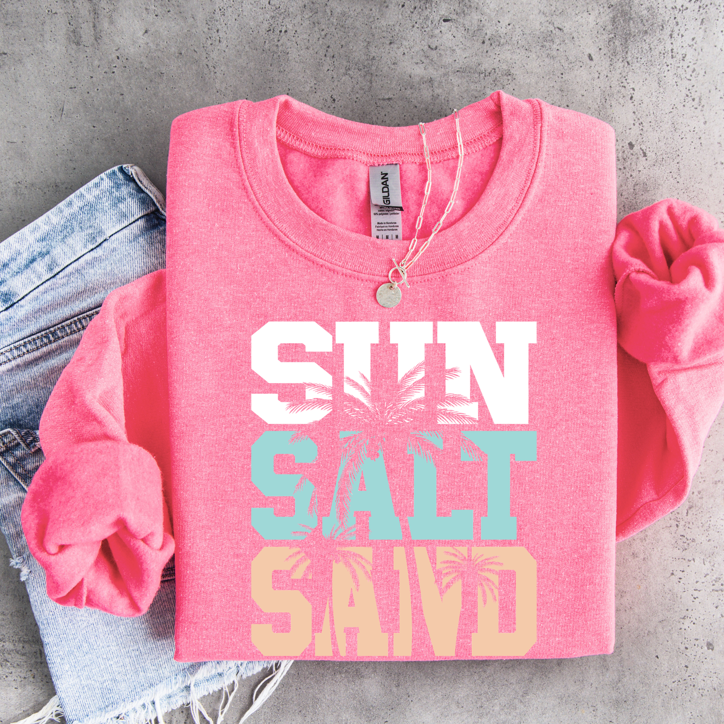 Pink sweatshirt with 'Sun Salt Sand' text on a concrete surface