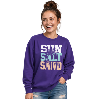 Side-by-side views of a woman wearing a purple crewneck sweatshirt with a stacked Sun Salt Sand graphic in white, aqua, and peach with dark palm trees.