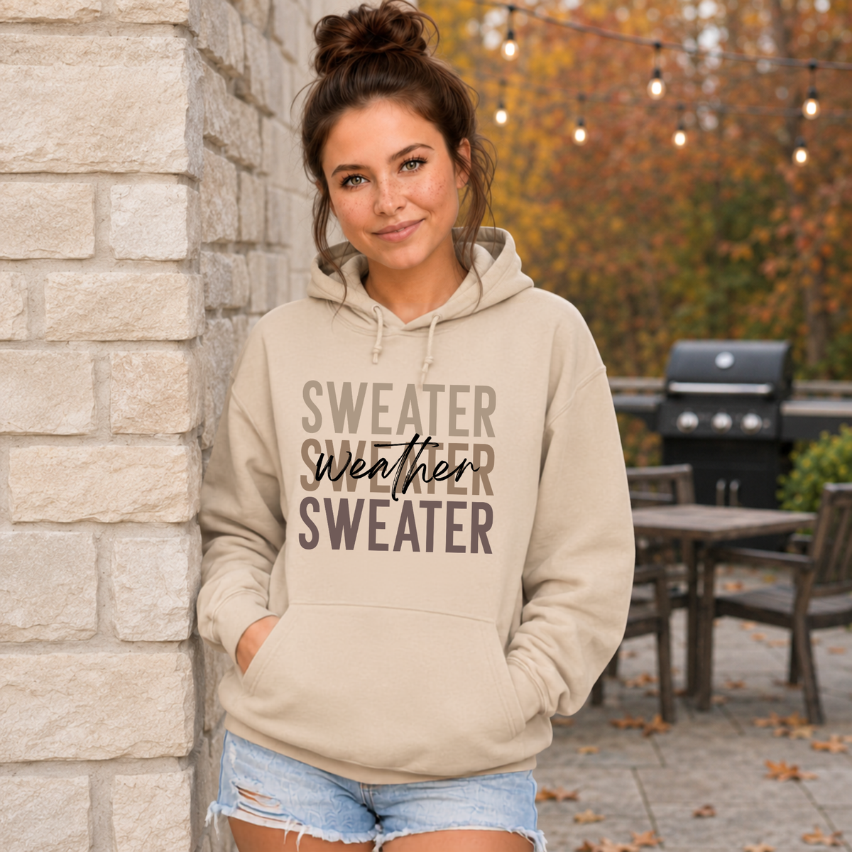 Woman outdoors wearing a sand-colored “Sweater Weather Sweater” crewneck hoodie with denim shorts.
