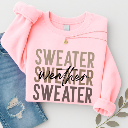 “Light pink Sweater Weather sweatshirt folded with necklace and jeans. A cozy and stylish unisex crewneck perfect for women’s fall outfits and winter layering.