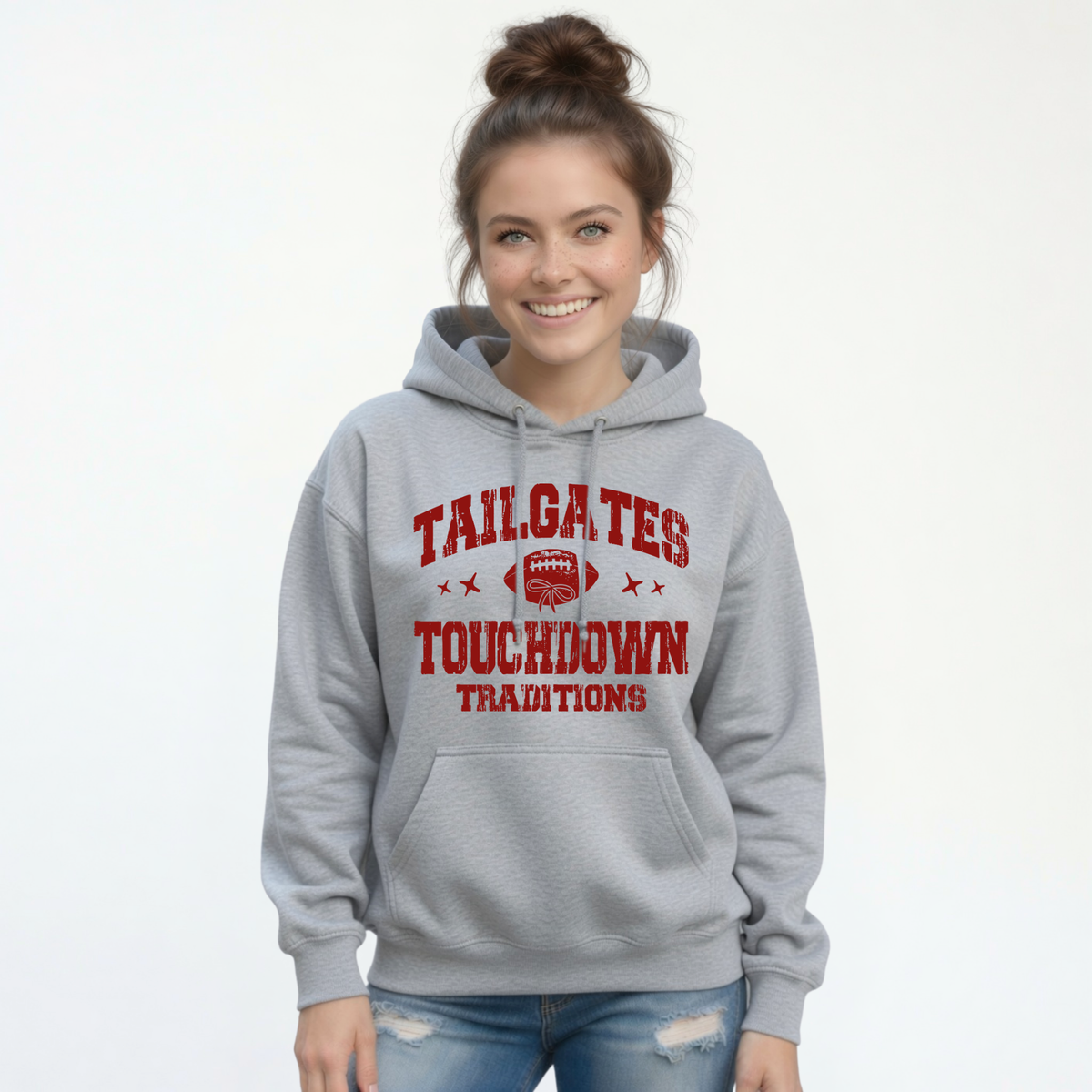 Sports gray hoodie with the Tailgates & Touchdown Traditions football design modeled by a woman in distressed jeans.