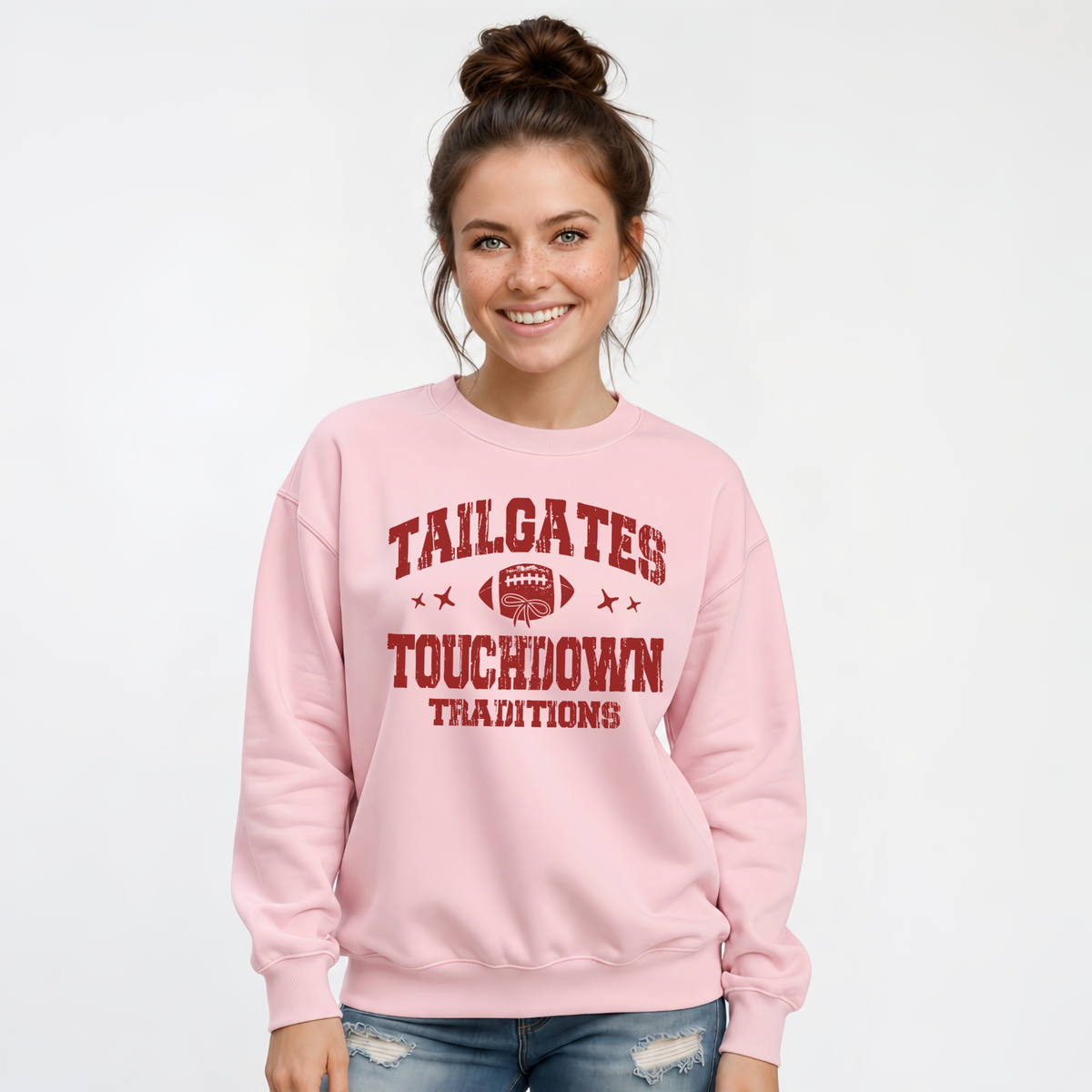 Smiling woman wears a light pink sweatshirt printed with the Tailgates & Touchdown Traditions football graphic.