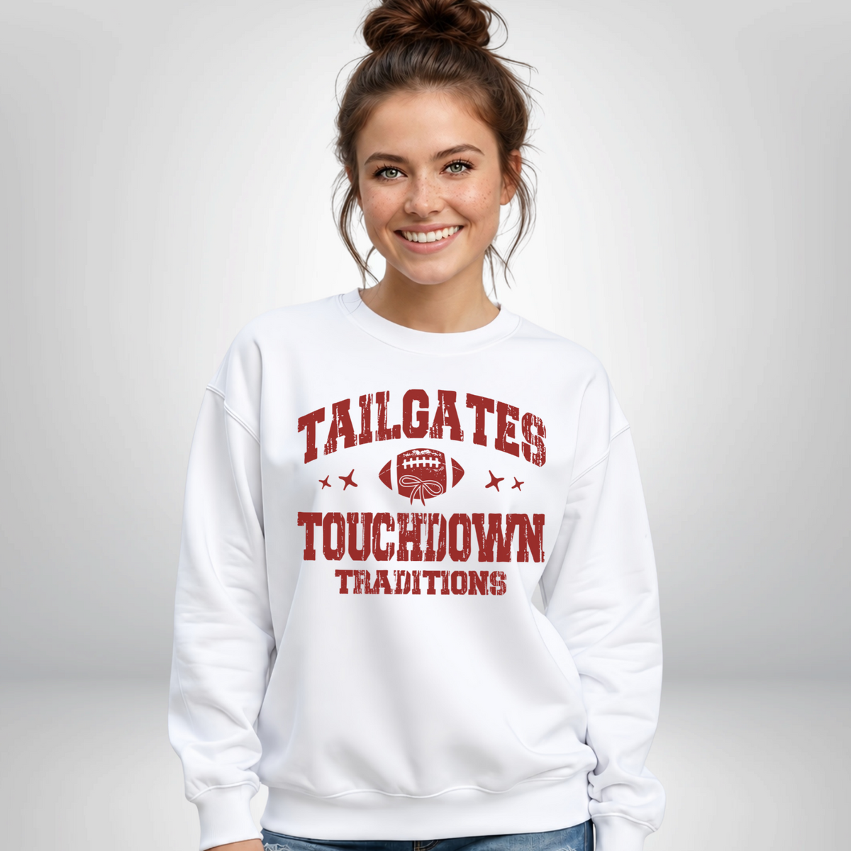 White crewneck sweatshirt displays the Tailgates & Touchdown Traditions design on a smiling woman in a bright studio.