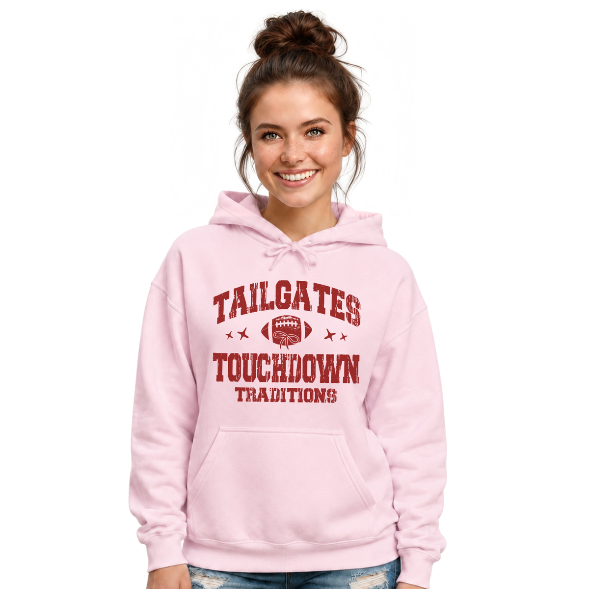 Smiling woman wears a light pink hoodie printed with the Tailgates & Touchdown Traditions football graphic.