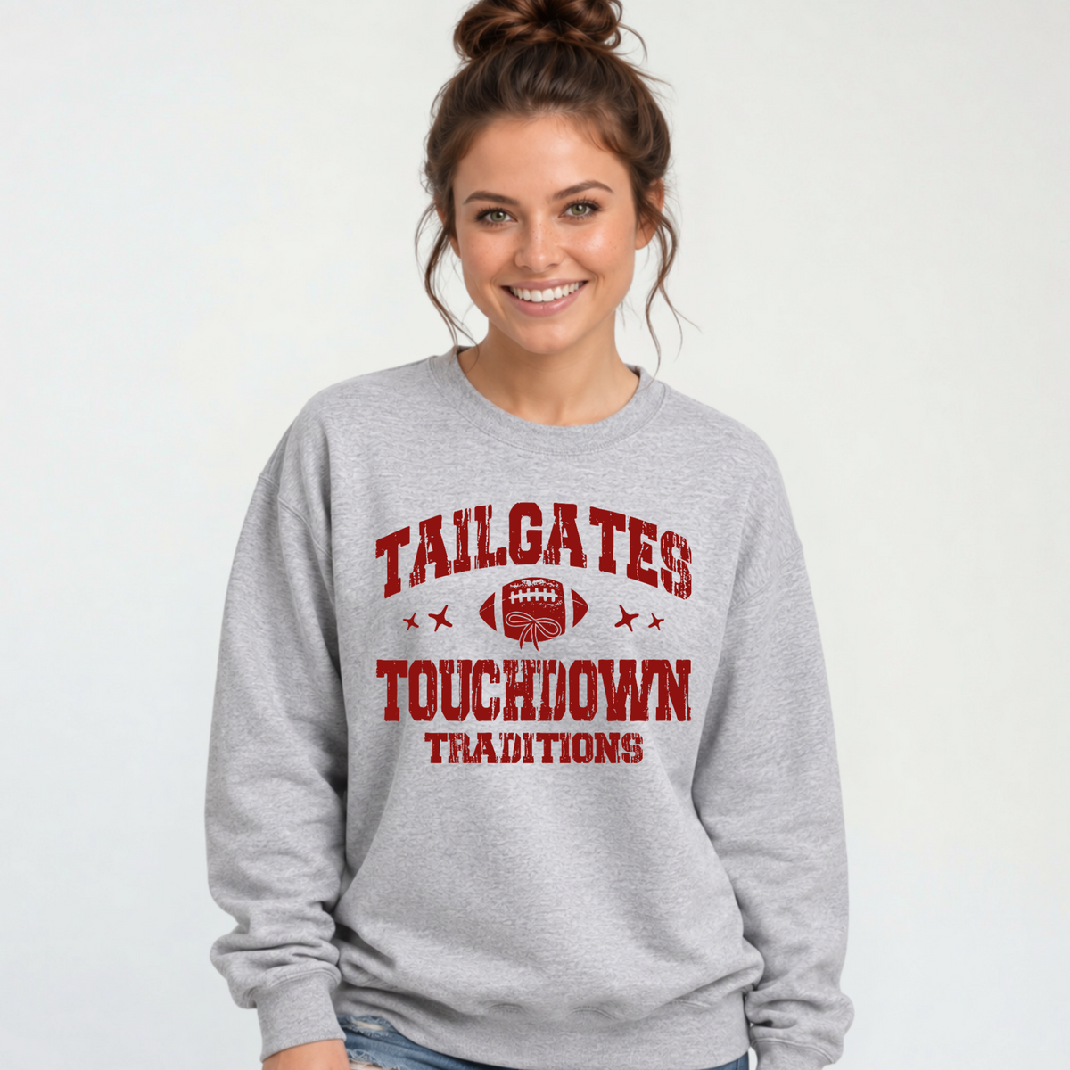 Sports gray crewneck sweatshirt with a red football and Tailgates & Touchdown Traditions wording, modeled with distressed jeans.