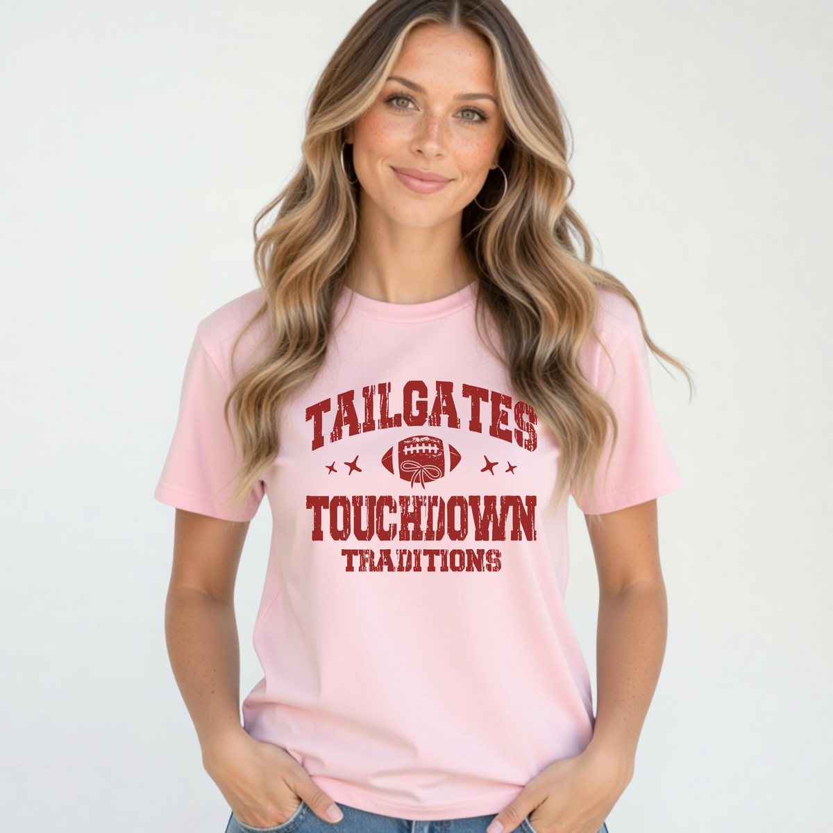 Light pink T-shirt with the red Tailgates & Touchdown Traditions football design modeled by a woman in jeans.