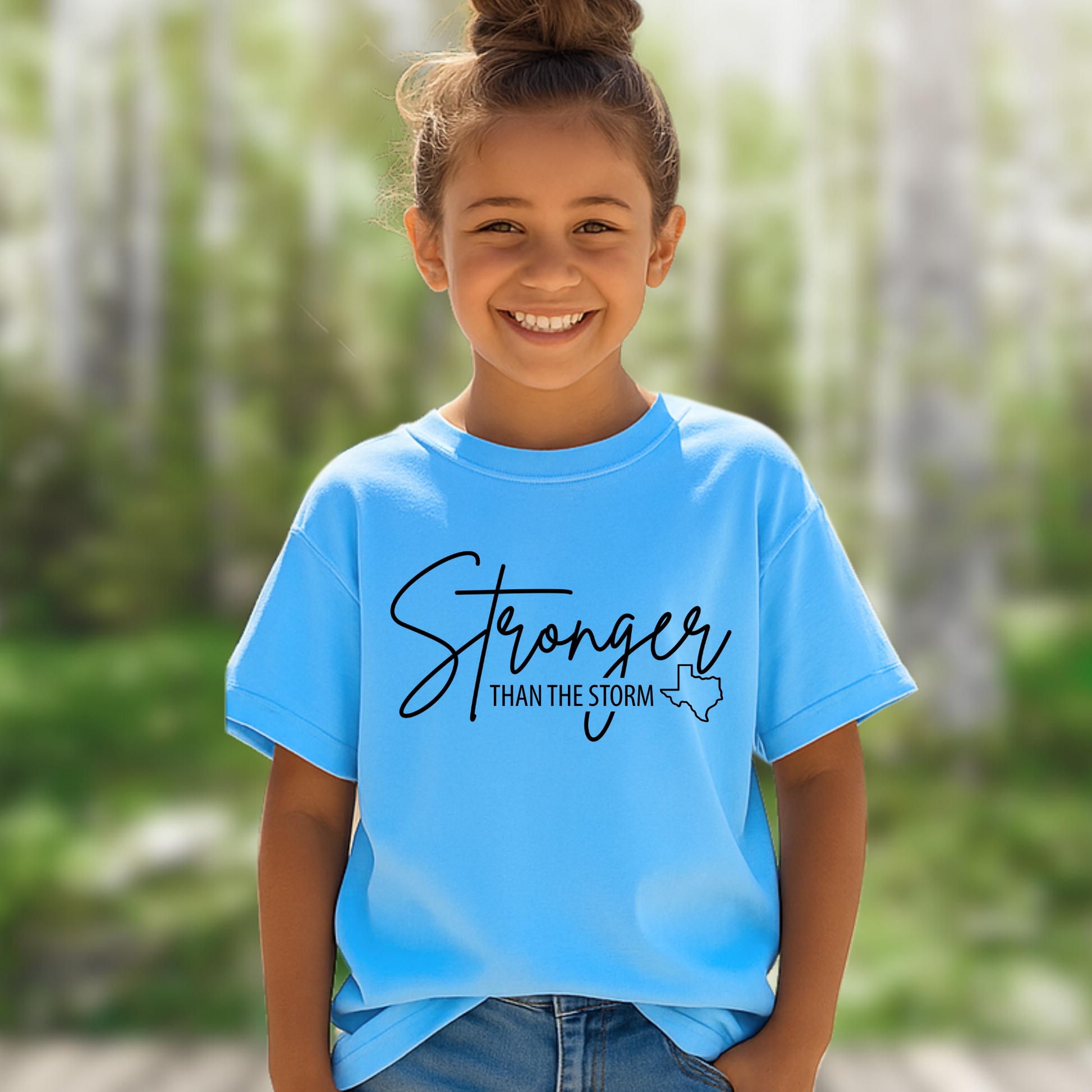 Sky blue youth “Stronger Than the Storm” tee, Christian flood relief shirt with Texas state outline, worn outside in nature.