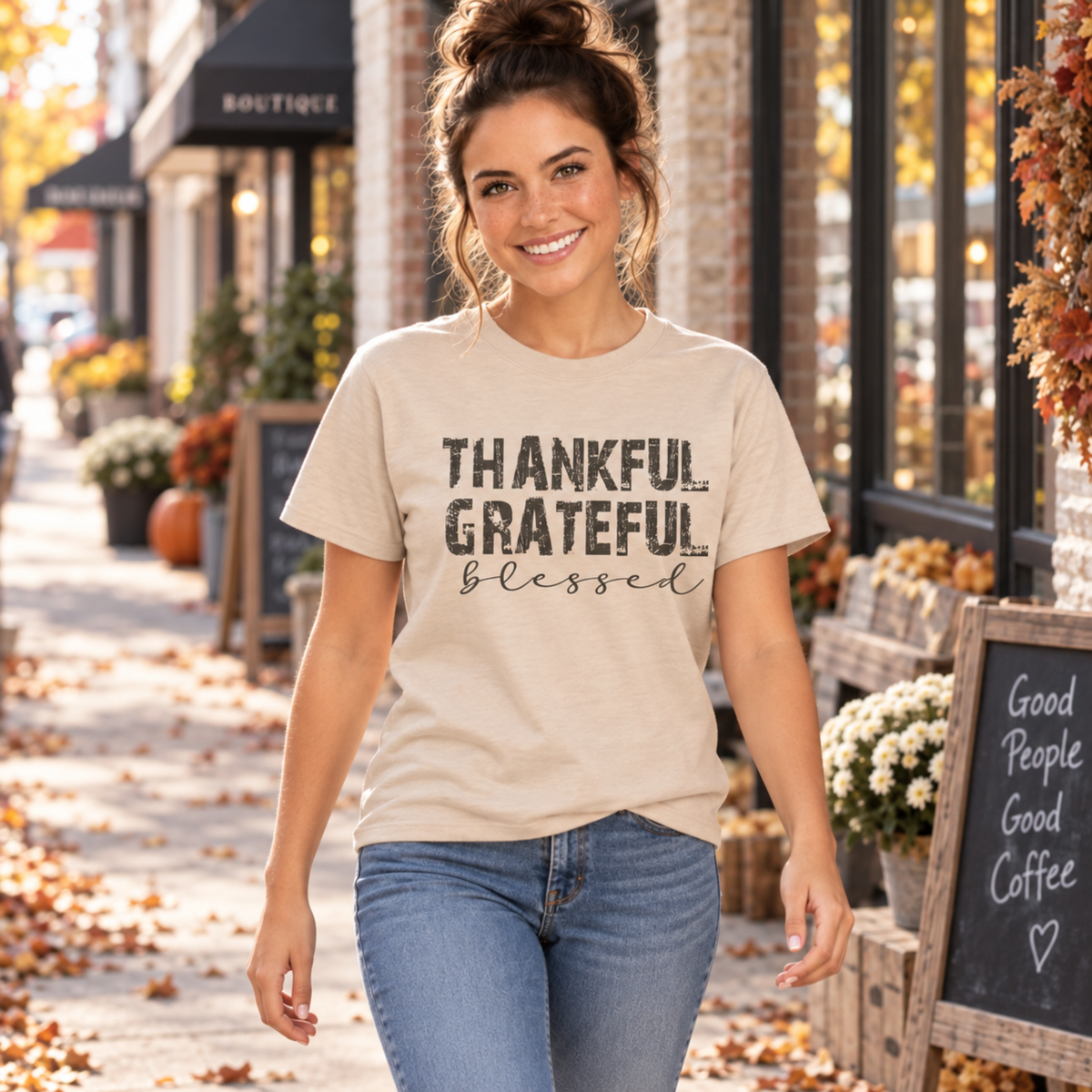 Woman wearing a sand T-shirt with distressed Thankful Grateful Blessed lettering outside a fall storefront.
