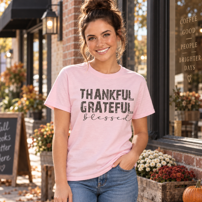 Woman wearing a light pink T-shirt with distressed Thankful Grateful Blessed lettering outside a fall cafe.