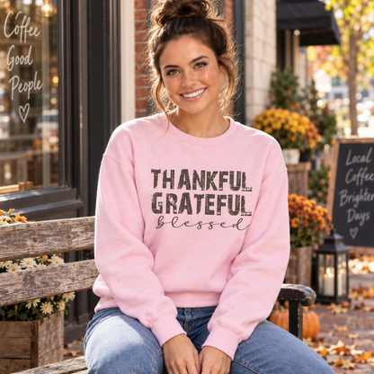 Woman seated in a light pink sweatshirt with Thankful Grateful Blessed text outside a fall coffee shop.