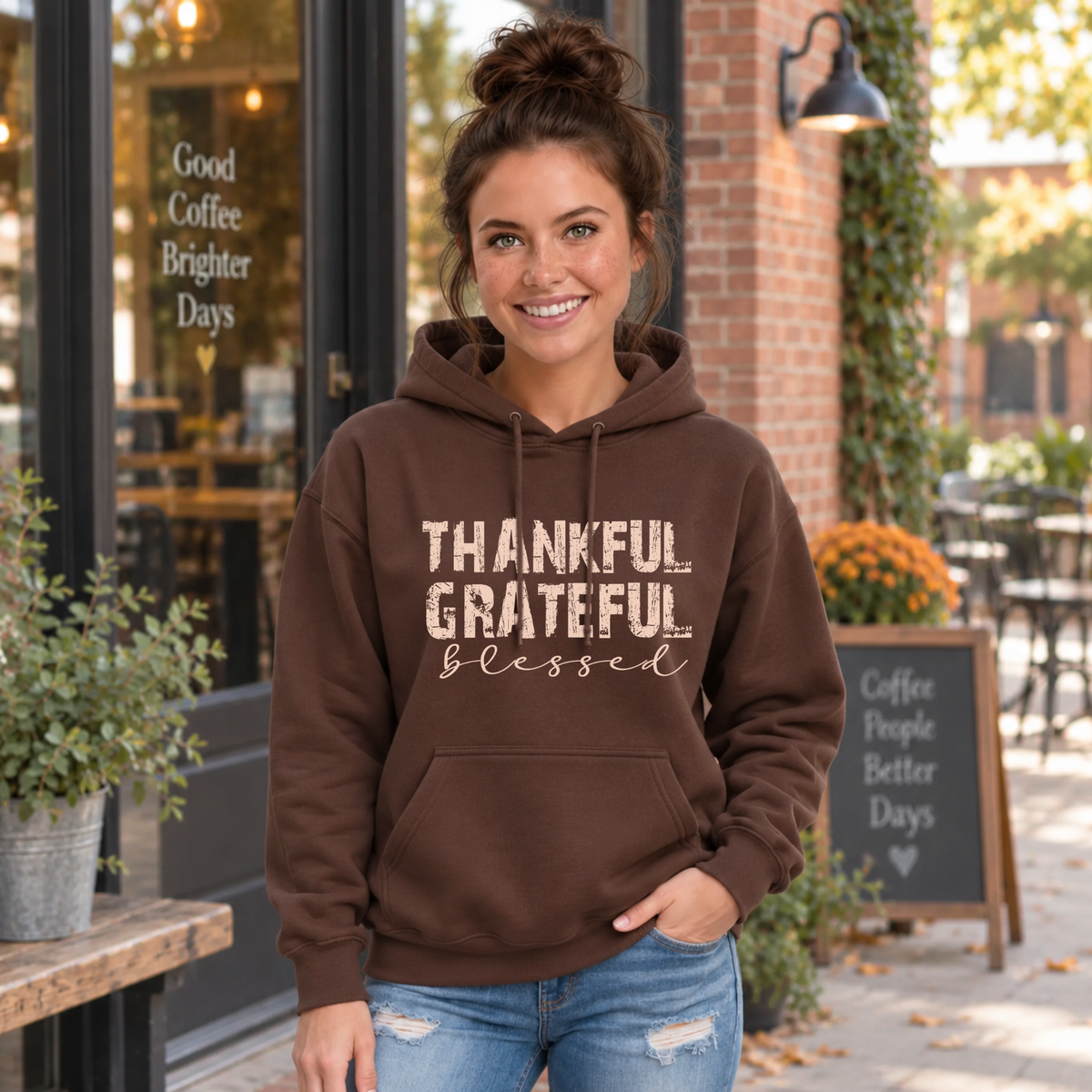 Woman wearing a brown hoodie with distressed Thankful Grateful Blessed lettering outside a fall cafe.