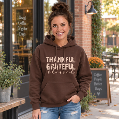 Woman wearing a brown hoodie with distressed Thankful Grateful Blessed lettering outside a fall cafe.