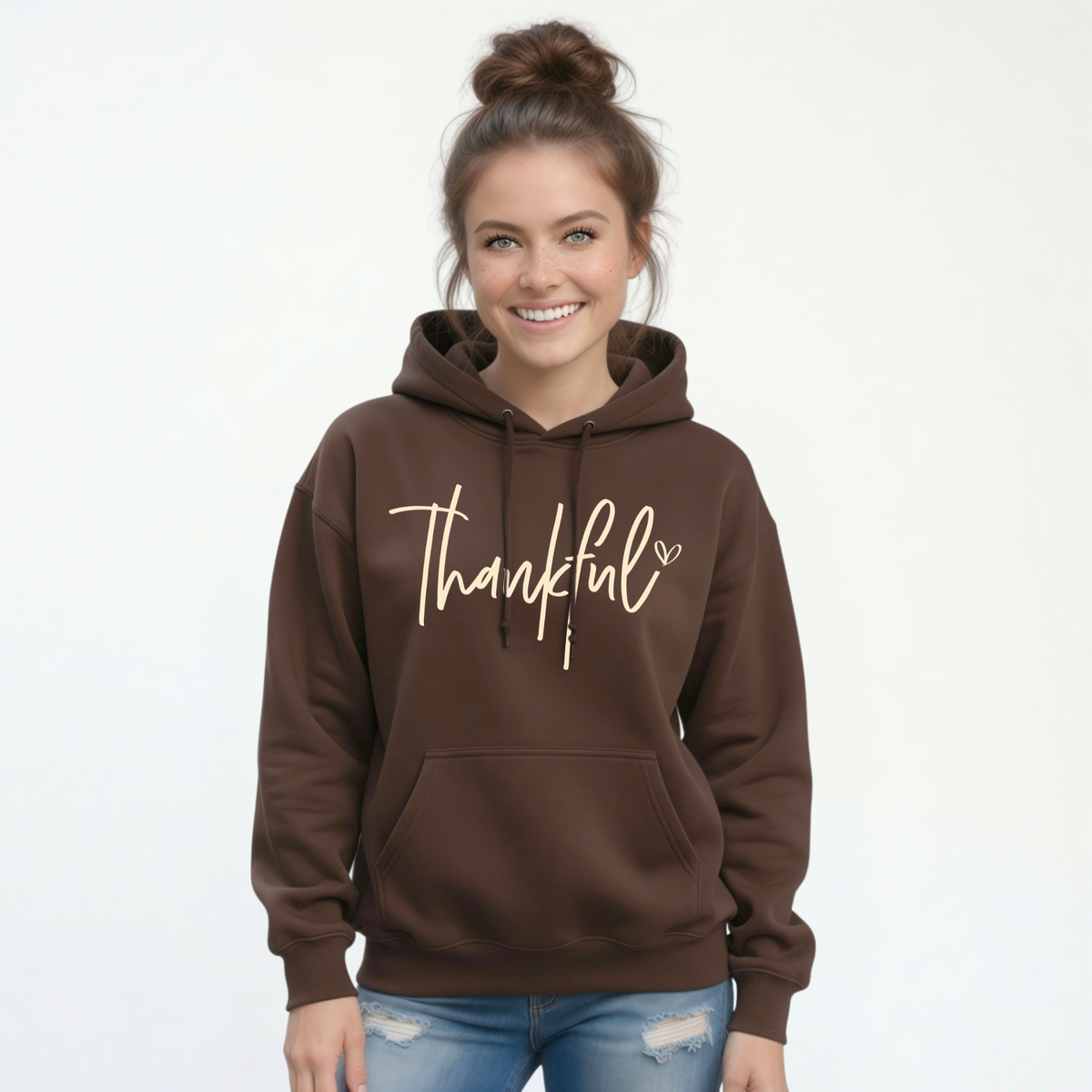 Woman wearing a brown pullover hoodie with a white Thankful script design and blue jeans