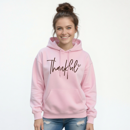 Woman wearing a light pink pullover hoodie with a white Thankful script design and blue jeans